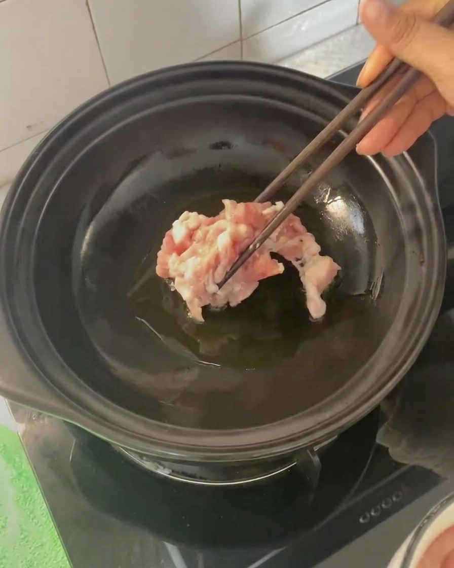 Tiras de panceta siendo añadidas a la cazuela caliente con palillos.