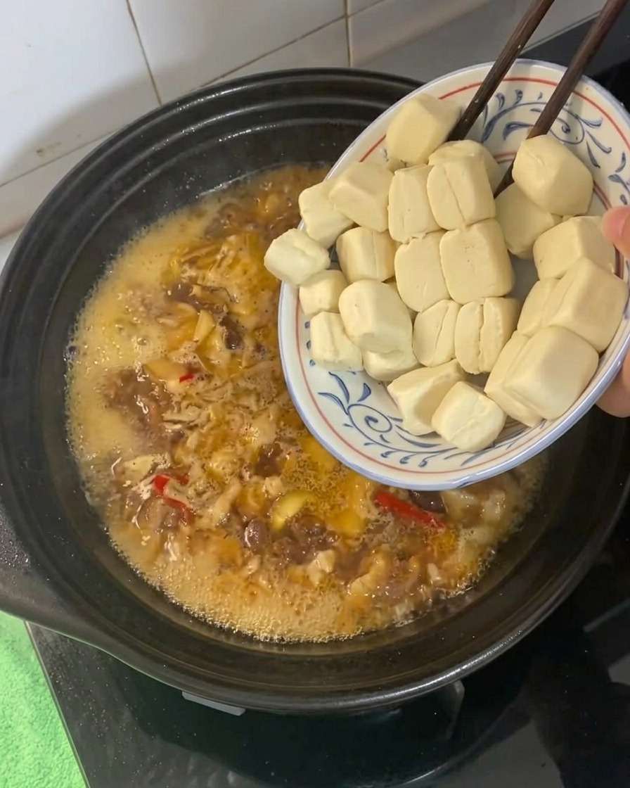 Cubos de tofu siendo añadidos a un caldo de estofado burbujeante en una cazuela.