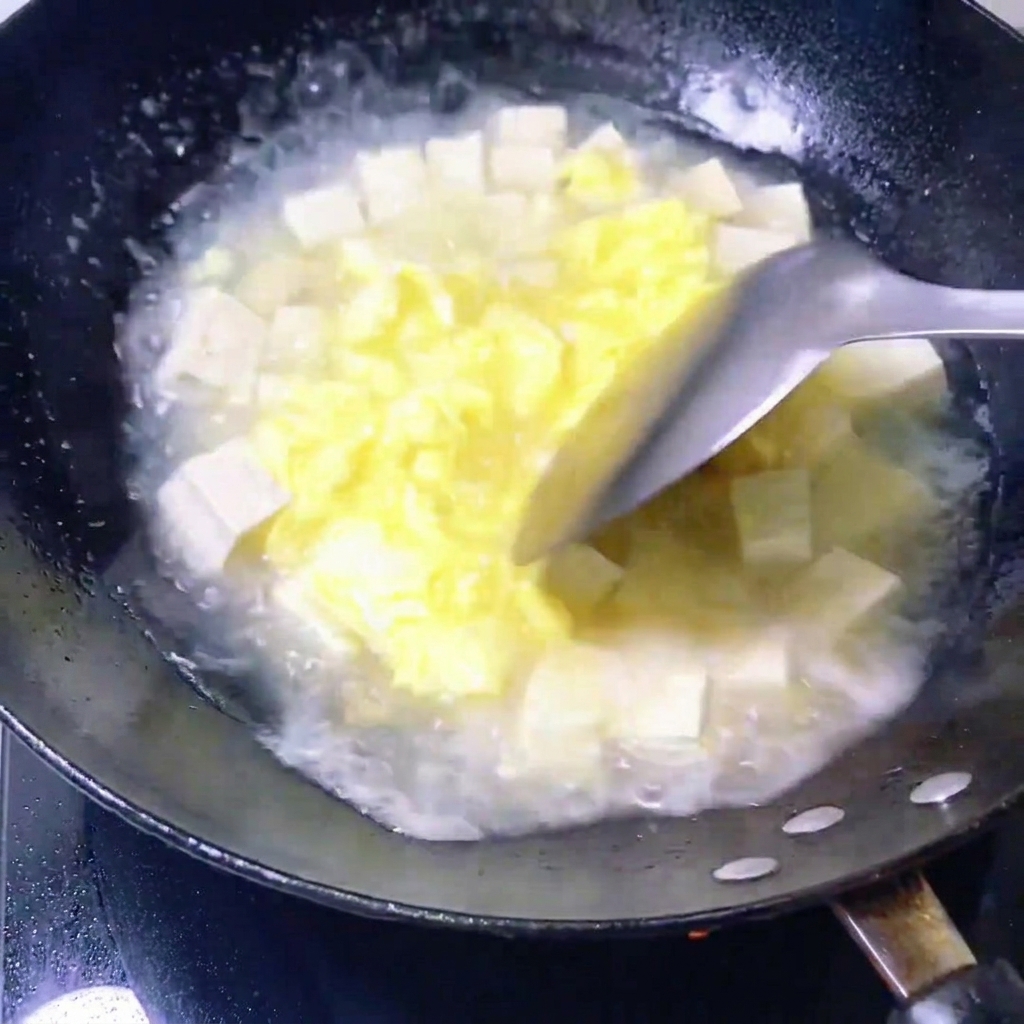 Almejas frescas siendo colocadas en una sartén con una mezcla de caldo de huevo y cubos de tofu.