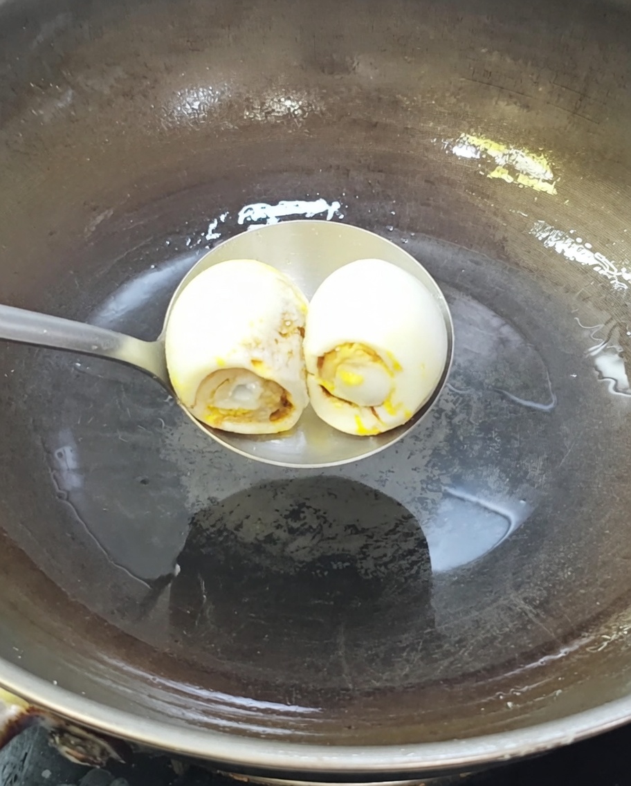 Dos huevos de pato salados friéndose en un wok caliente con aceite.