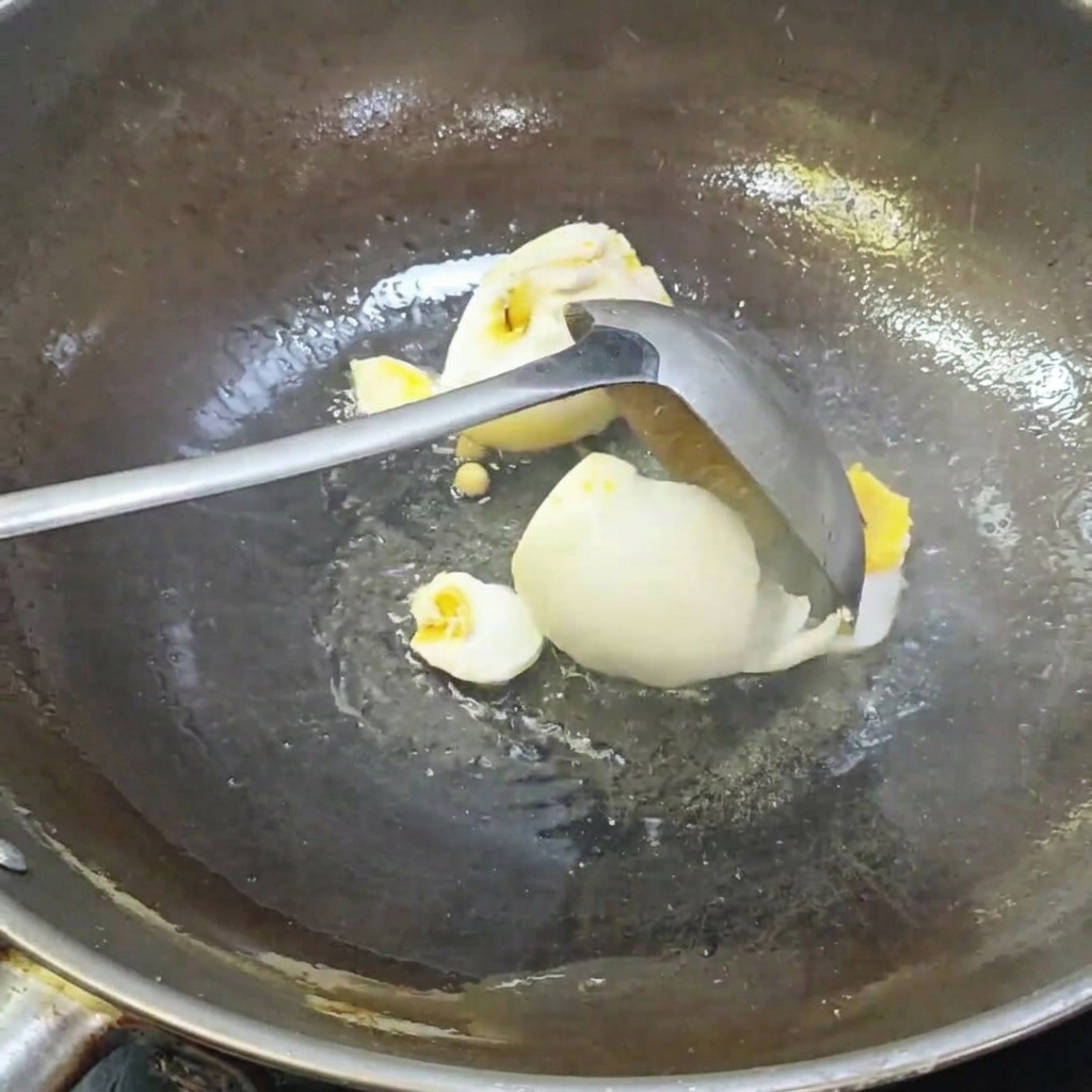 Un cucharón rompiendo los huevos de pato salados en un wok.