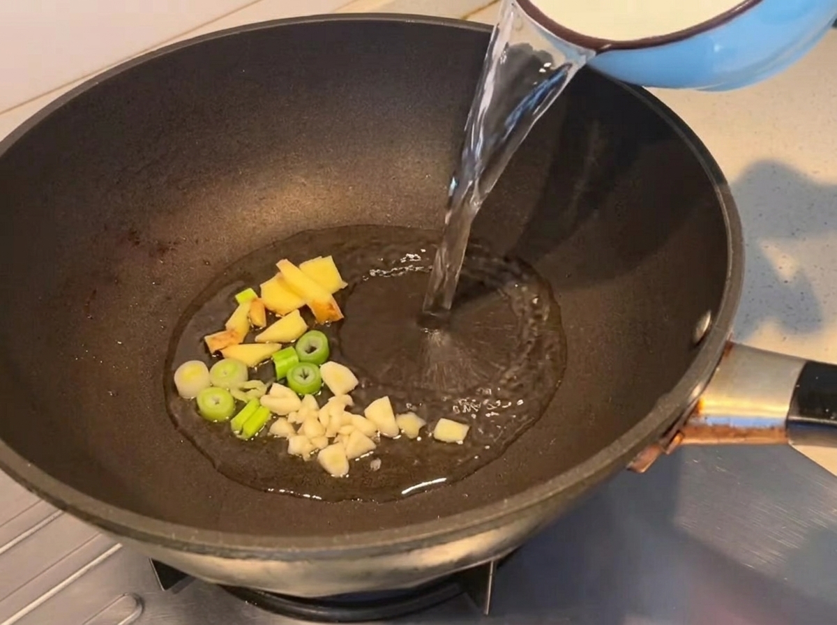 Agua vertiéndose en una sartén con aromáticos salteados.
