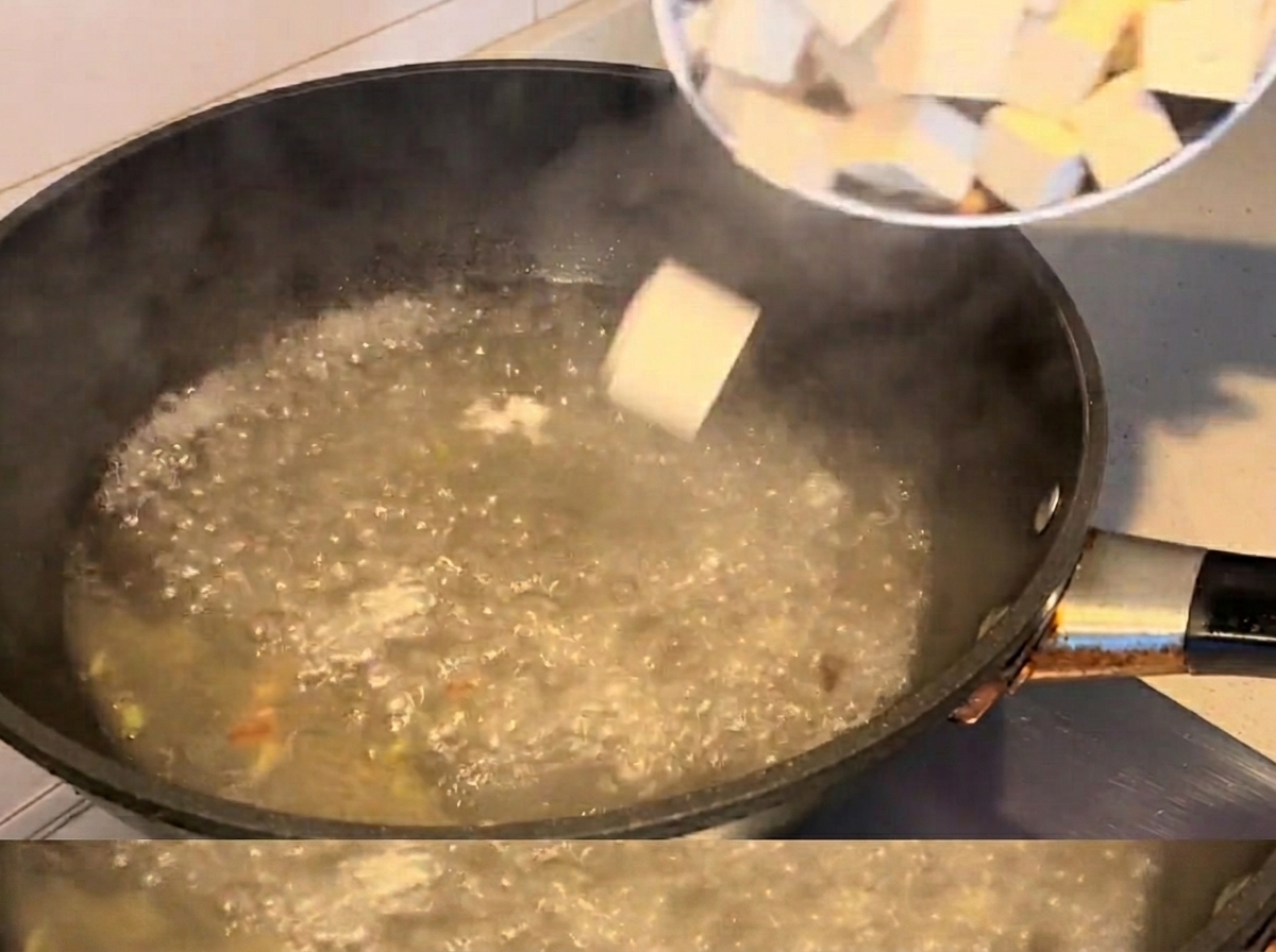 Cubos de tofu y almejas cocinándose en una sopa hirviendo.