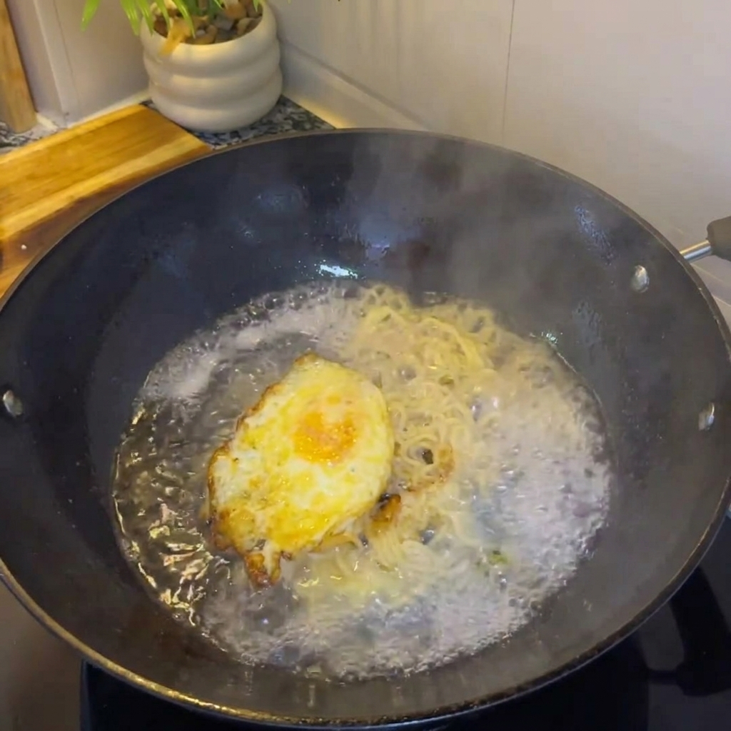 Agua caliente vertiéndose en el wok con el huevo y los cebollinos, creando un caldo.