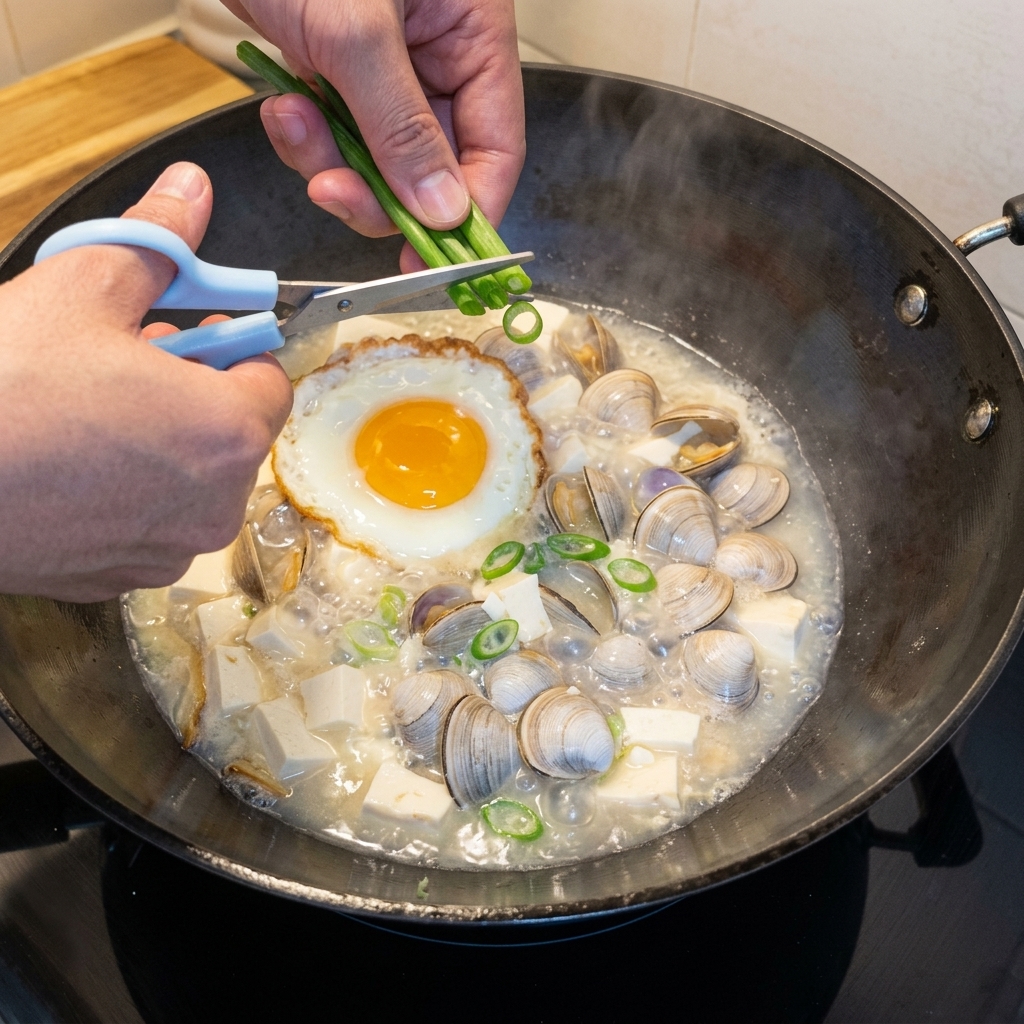 Cebollinos frescos picados espolvoreados sobre una olla burbujeante de sopa de tofu y almejas.