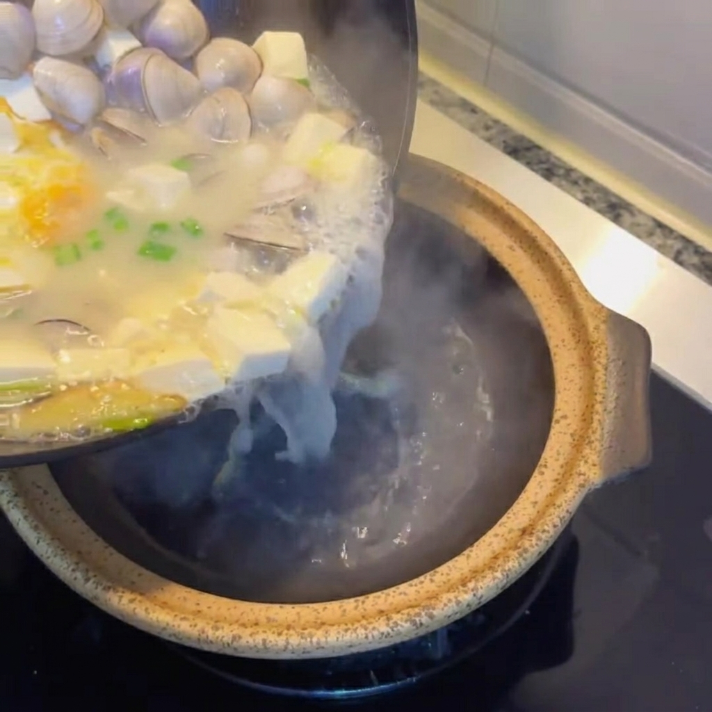 Sopa de tofu y almejas servida en una olla de barro rústica.