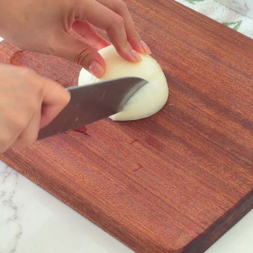 Media cebolla blanca siendo picada cuidadosamente sobre una tabla de madera.