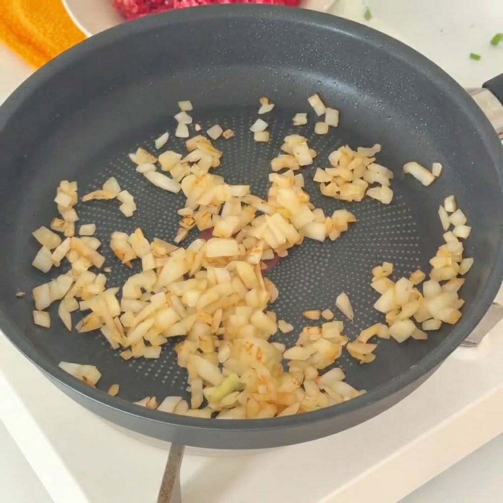 Las cebollas sofritas siendo transferidas a un tazón con carne picada fresca.
