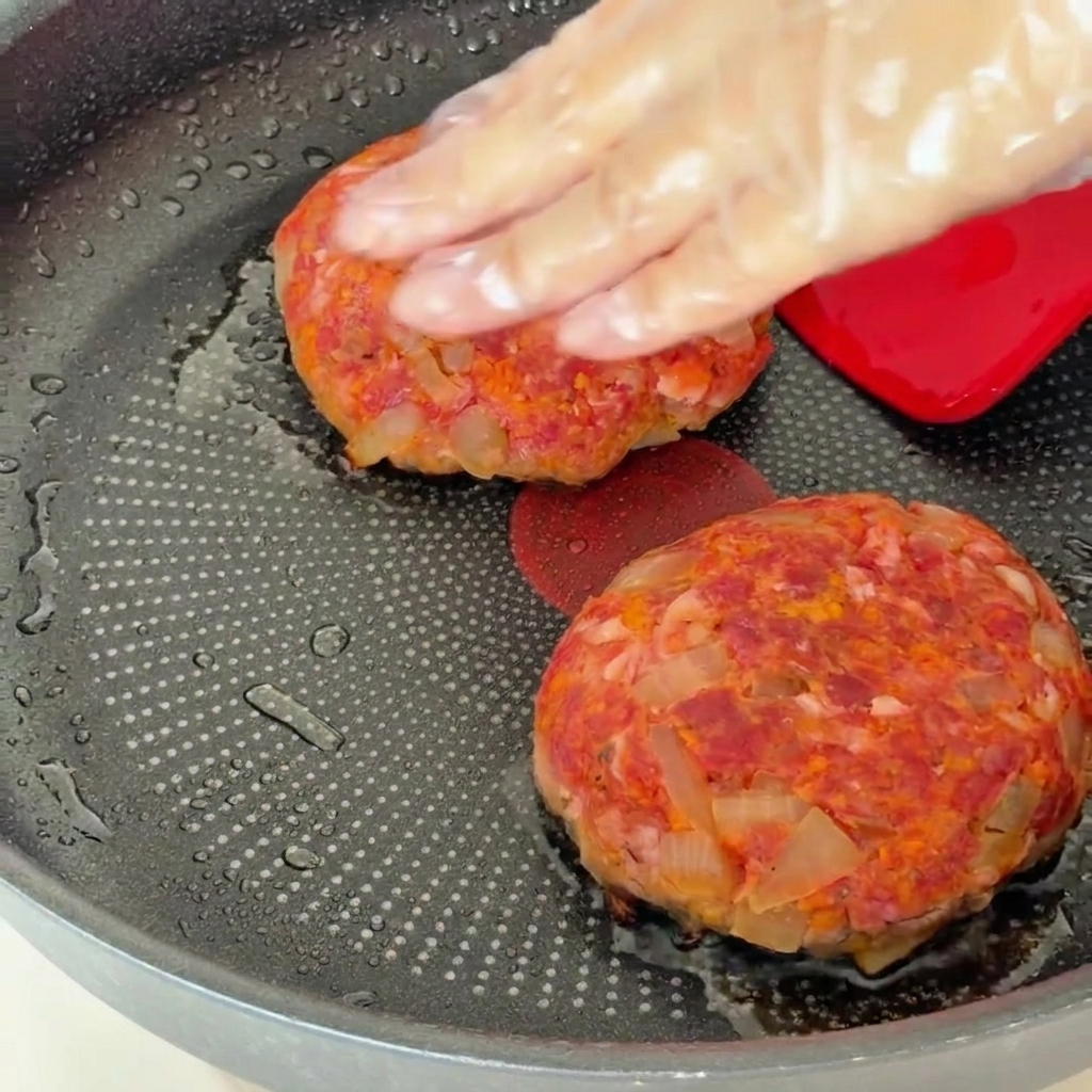 Hamburguesas en una sartén siendo cubiertas con una tapa tras darles la vuelta.