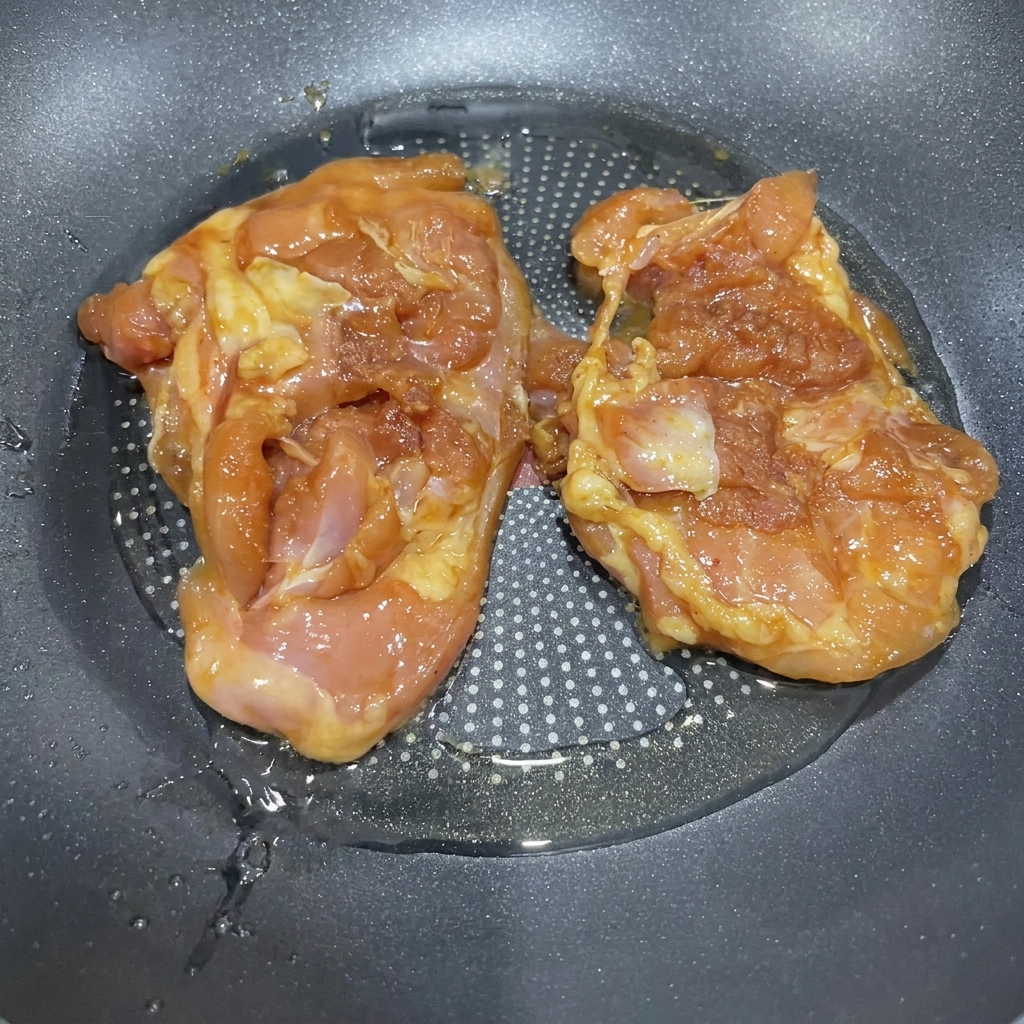 Muslos de pollo marinados sofriéndose en una sartén con aceite caliente.