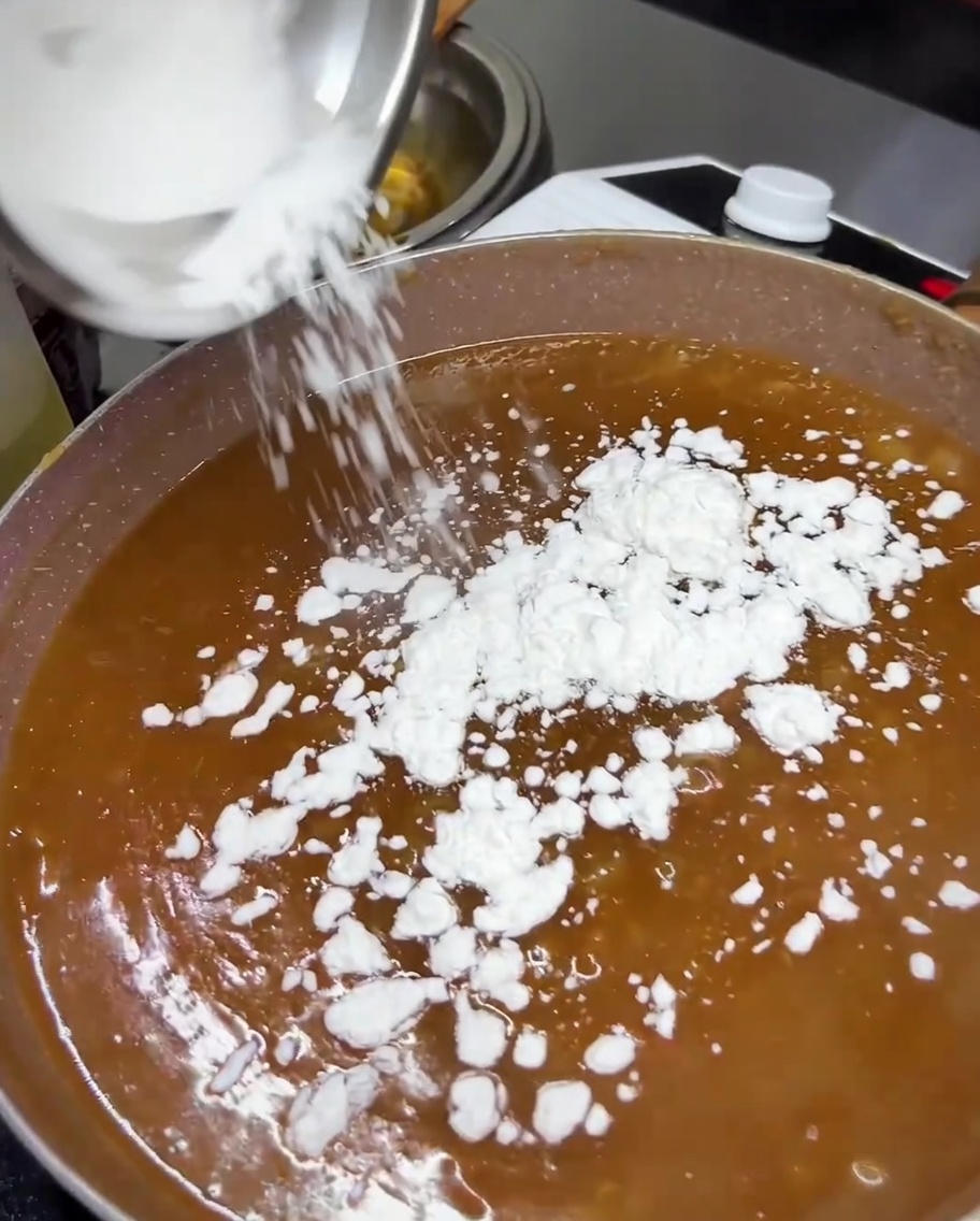 Almidón de tapioca siendo añadido a la salsa teriyaki a fuego lento en una sartén.