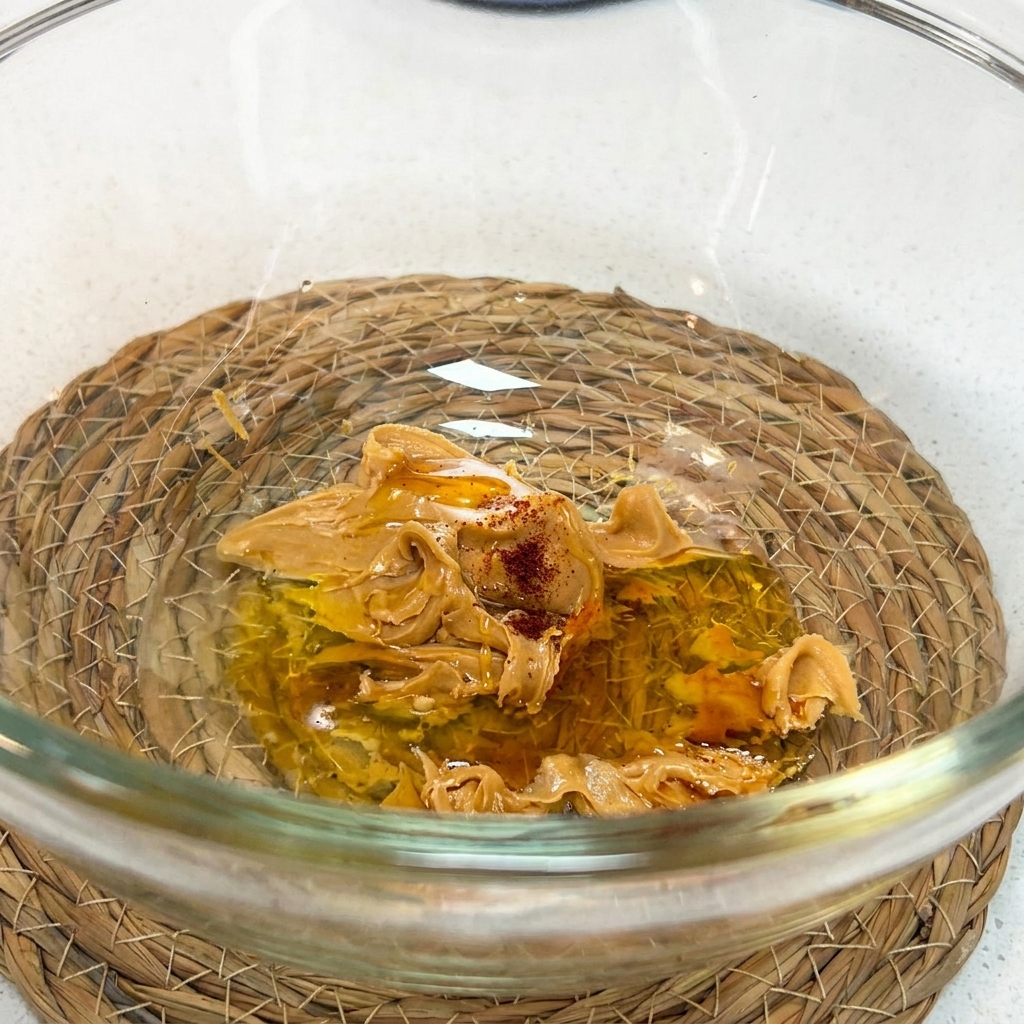 Unas varillas mezclando la crema de cacahuete, la salsa de soja, la miel, el vinagre, el agua y la salsa shacha en un cuenco de cristal.