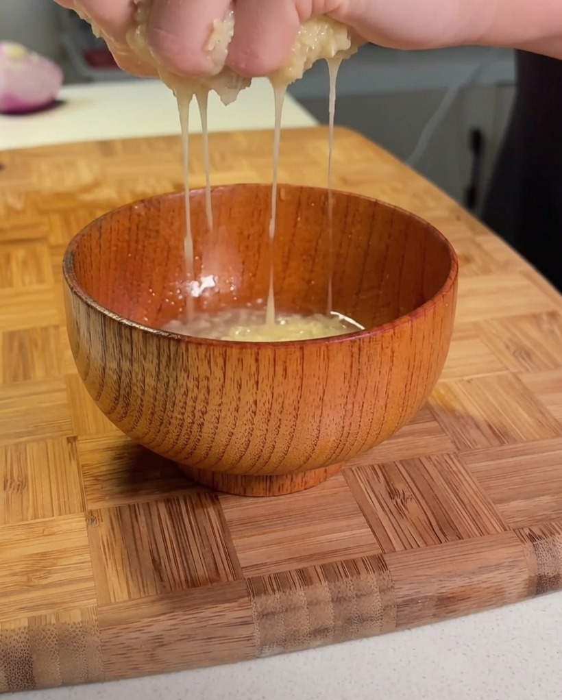 Manos escurriendo patata rallada sobre un pequeño cuenco de madera para extraer el líquido.