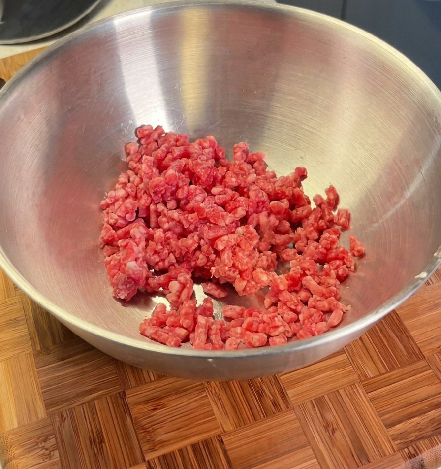 Carne picada en un cuenco metálico lista para ser sazonada con chalotas, sal y pimienta negra.