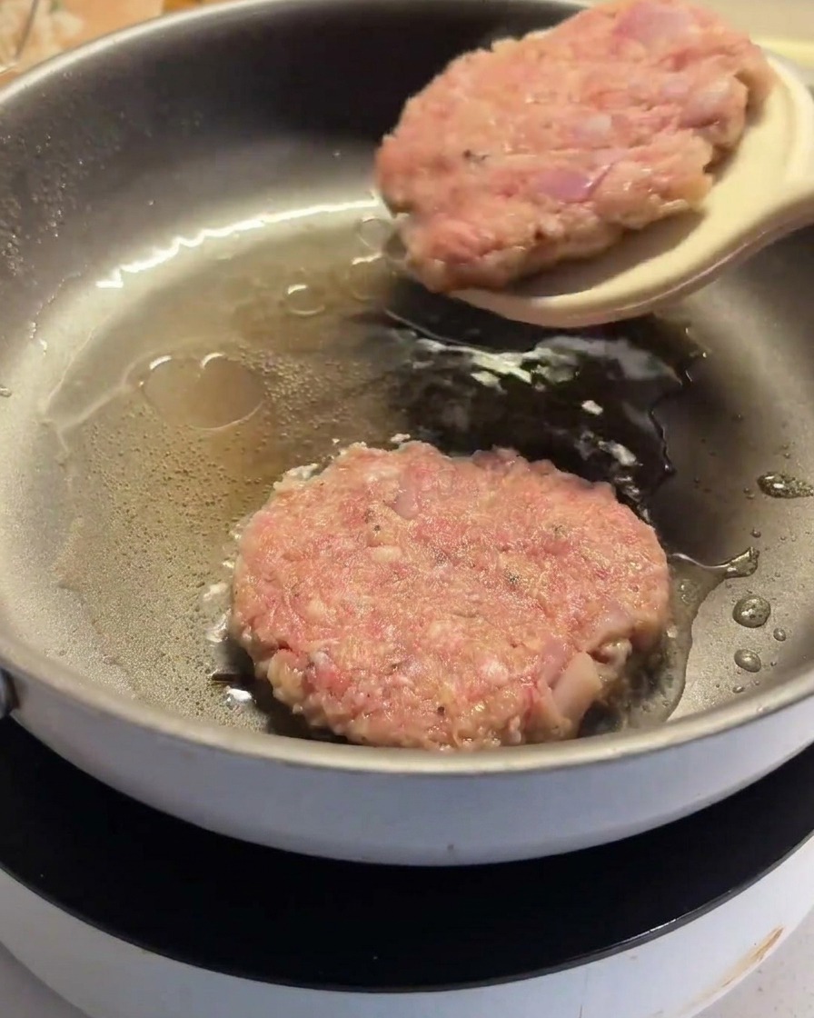 Una espátula dando la vuelta a una hamburguesa parcialmente cocinada en la sartén.