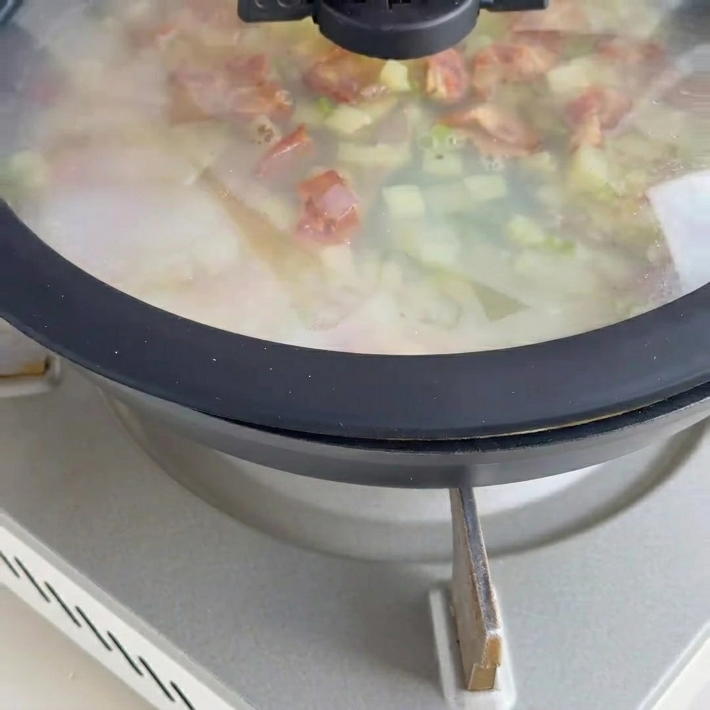 Sopa cremosa cocinándose con almejas y trozos de tocino encima.