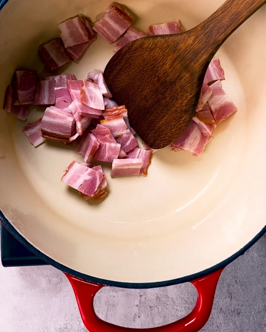 Trozos de tocino dorándose en una olla de hierro fundido esmaltado.