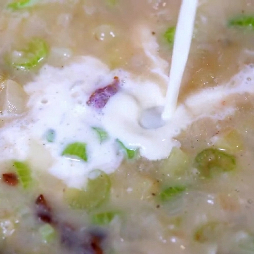 Añadiendo carne de almeja picada a la sopa cremosa burbujeante.