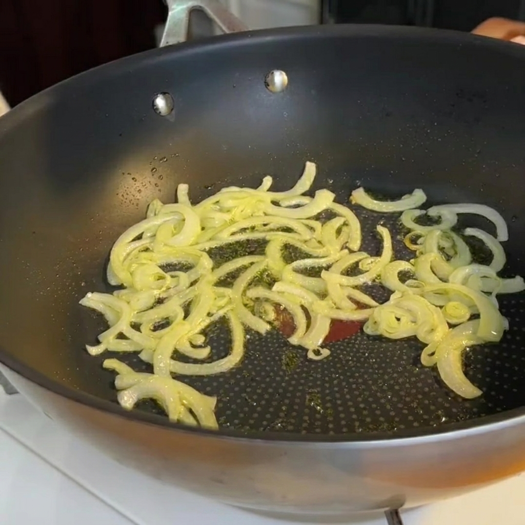 Trozos de tallos de espárrago siendo añadidos a una sartén con cebollas sofritas.