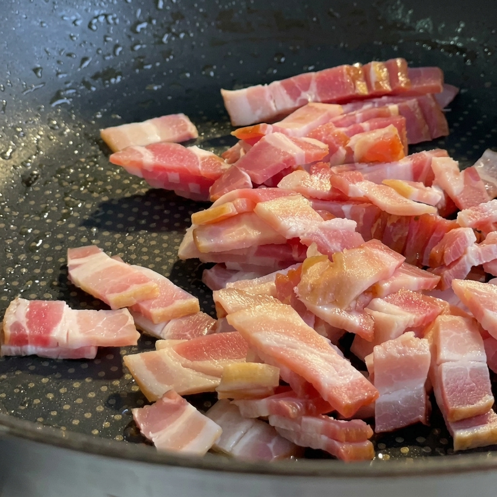 Trozos de panceta friéndose en una sartén hasta quedar dorados y crujientes.
