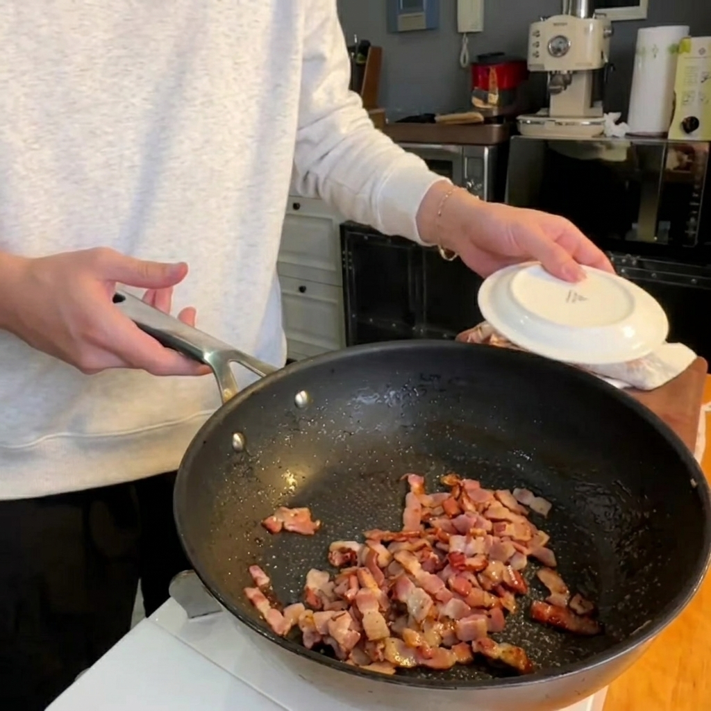 Puntas de espárrago friéndose en una sartén junto a trozos de panceta crujiente.