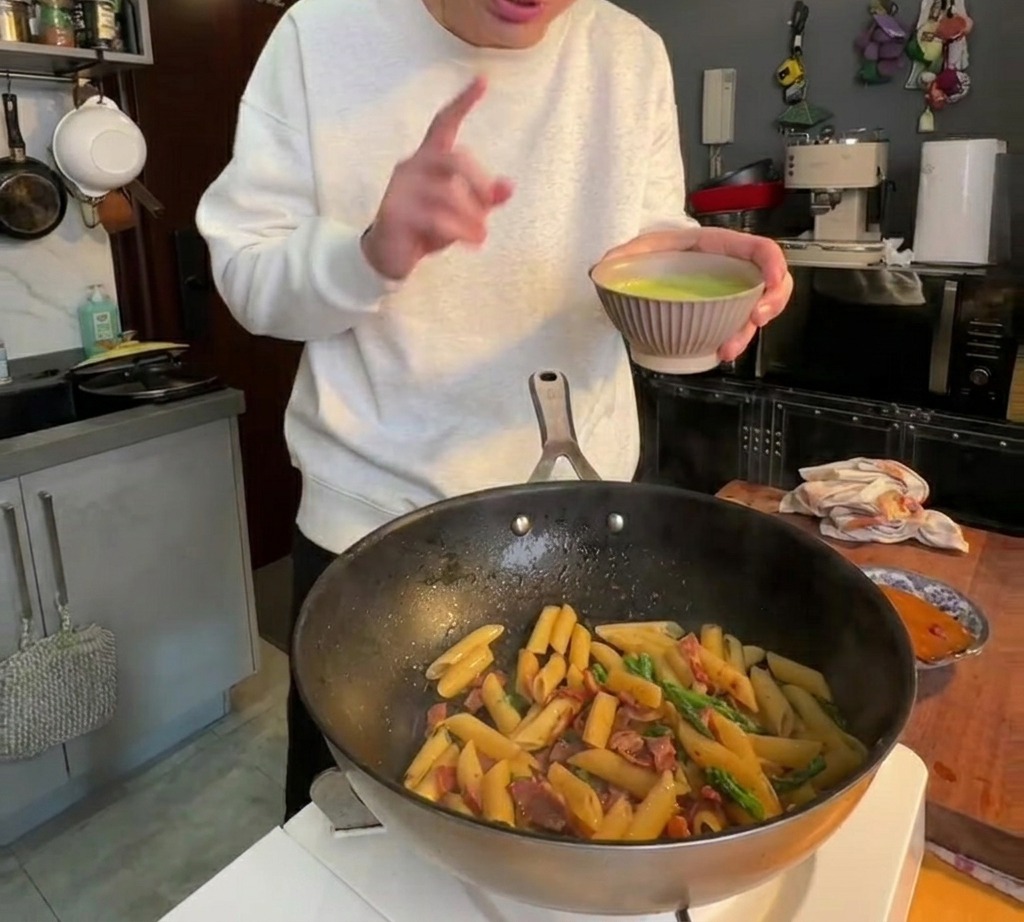Salsa de espárragos verde y suave siendo vertida sobre pasta penne en una sartén.