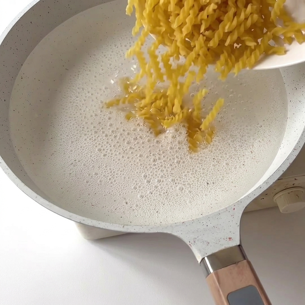 Pasta fusilli cayendo en una olla de agua hirviendo.