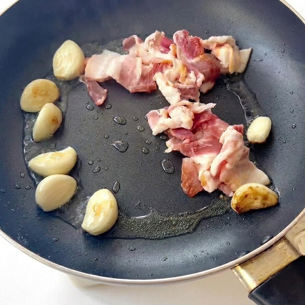 Bacon friéndose en una sartén junto con los dientes de ajo dorados.