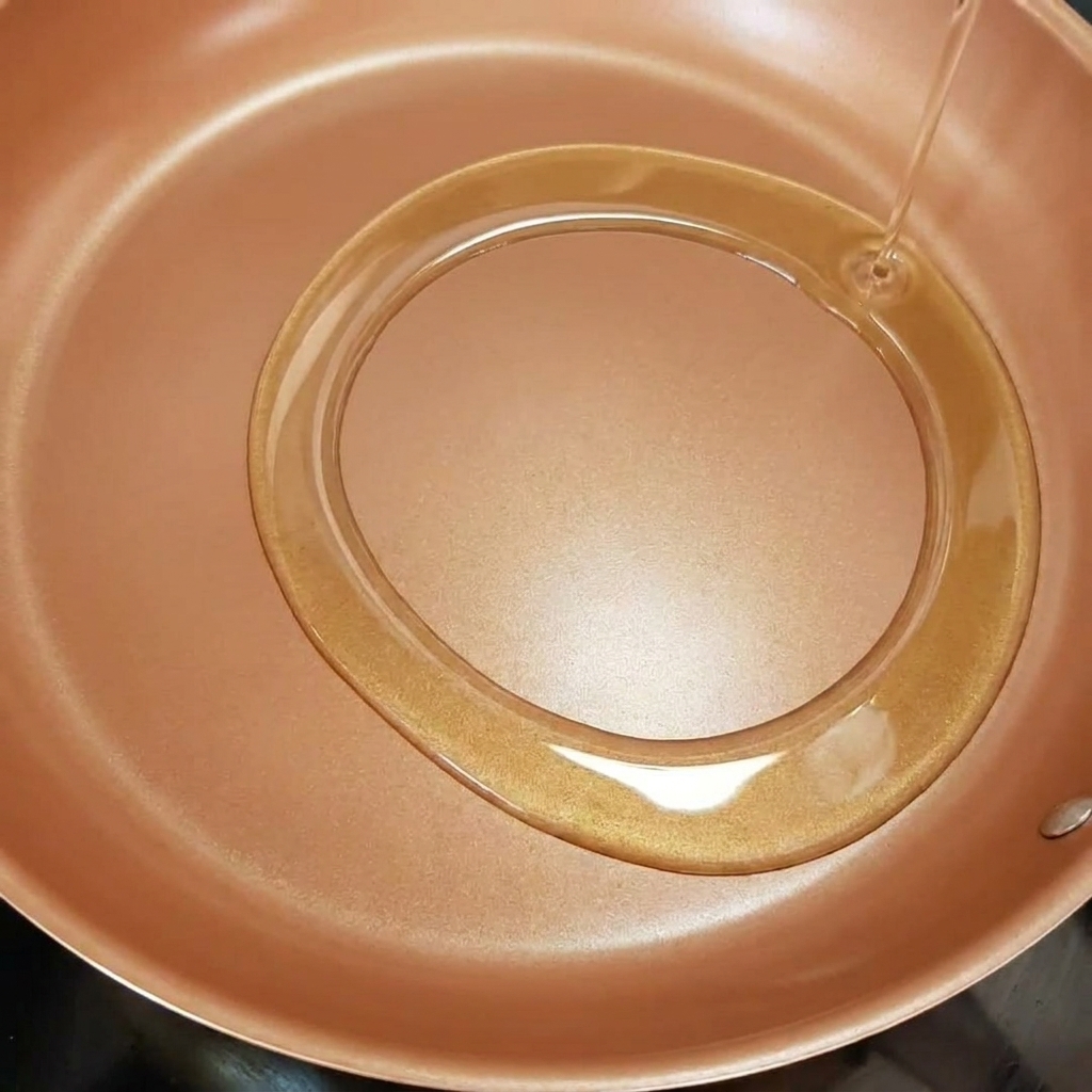 Tiras de cebolla friéndose en una sartén con aceite de oliva caliente brillante.