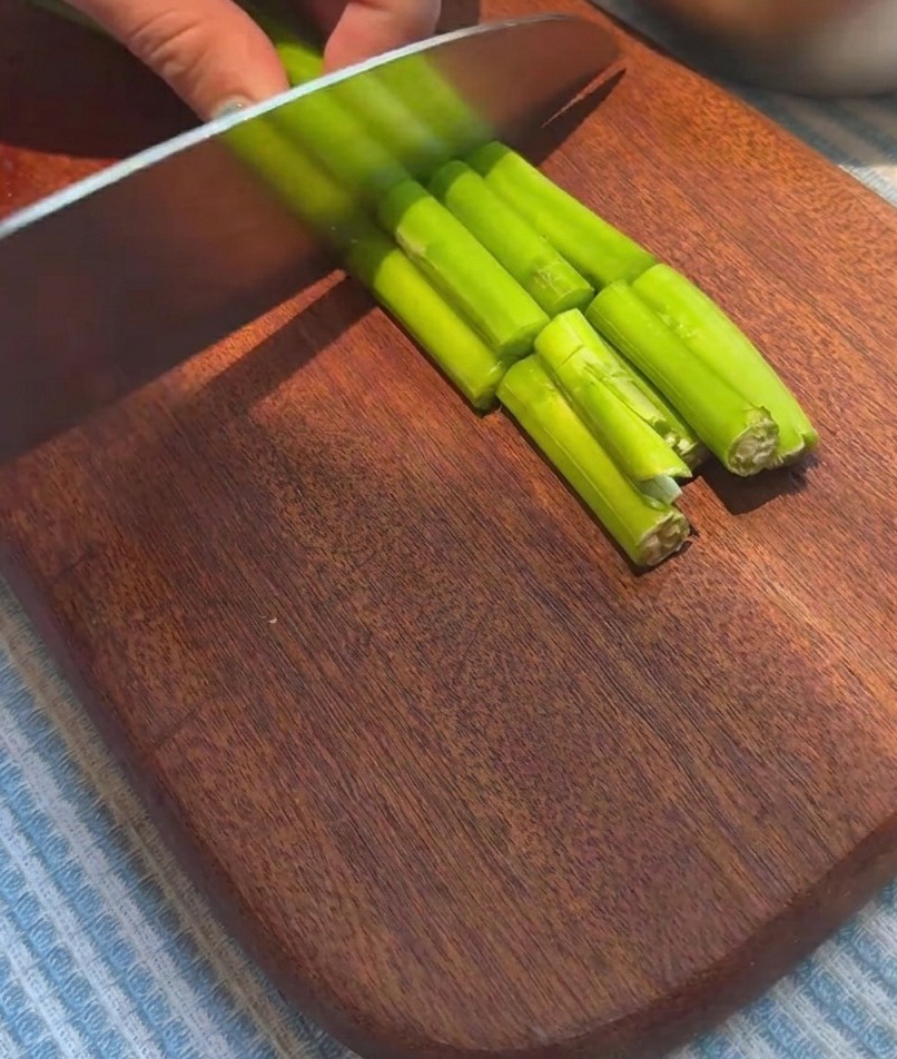 Espárragos frescos cortados en trozos uniformes sobre una tabla de cortar de madera.