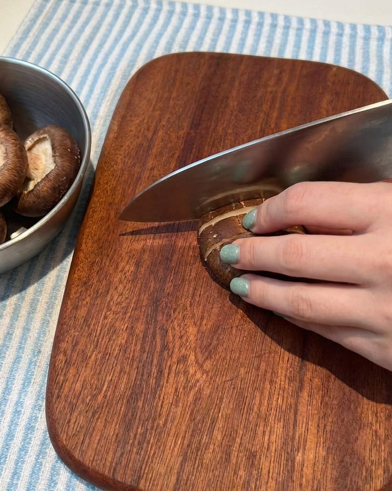 Champiñones frescos cortados cuidadosamente en láminas finas sobre una tabla de cortar de madera.