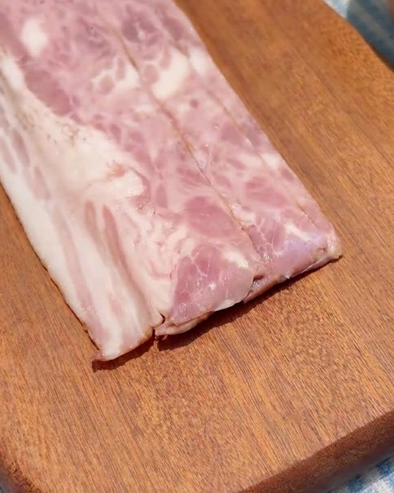 Tiras de tocino cortadas en cuadrados uniformes sobre una tabla de cortar de madera.