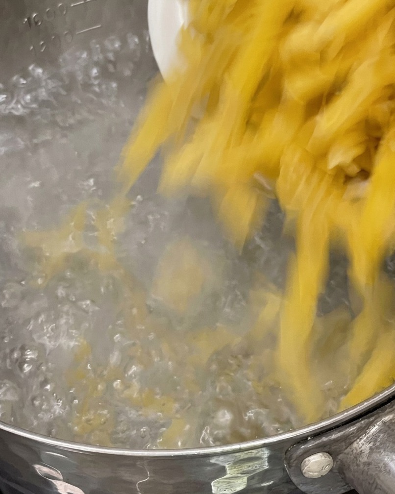 Pasta cruda siendo añadida a una olla con agua hirviendo burbujeante.