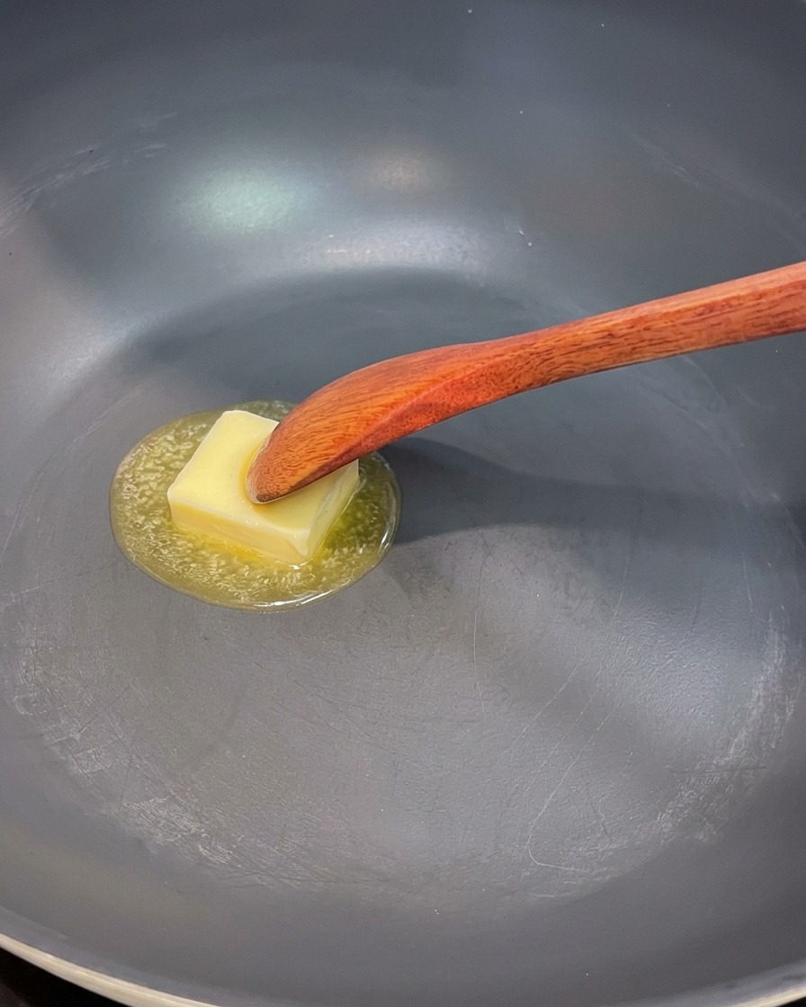 Una sartén con mantequilla derretida, cebolla roja, champiñones y trozos de espárragos salteándose.