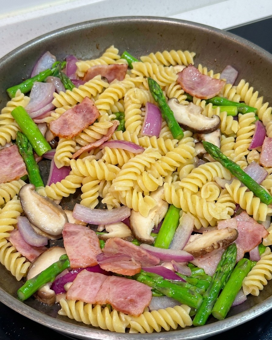 Pasta mezclándose con verduras y tocino en una sartén, siendo sazonada con pimienta negra y salsa de soja.