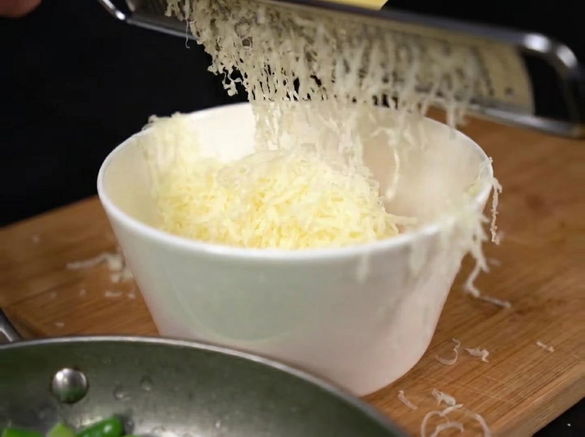 Queso parmesano recién rallado cayendo en un montón sobre las yemas de huevo en un bol.