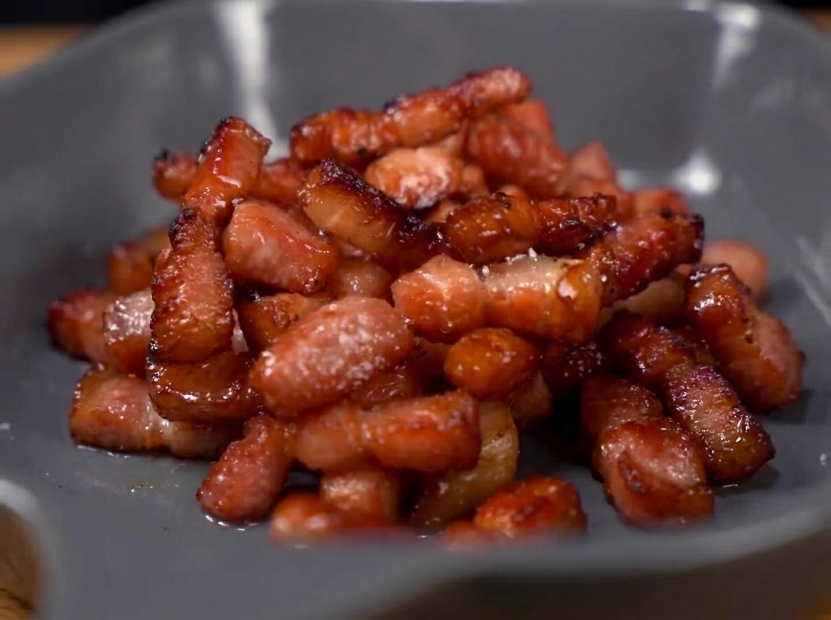 Espárragos y guisantes salteándose en una sartén con trozos de tocino cocido.