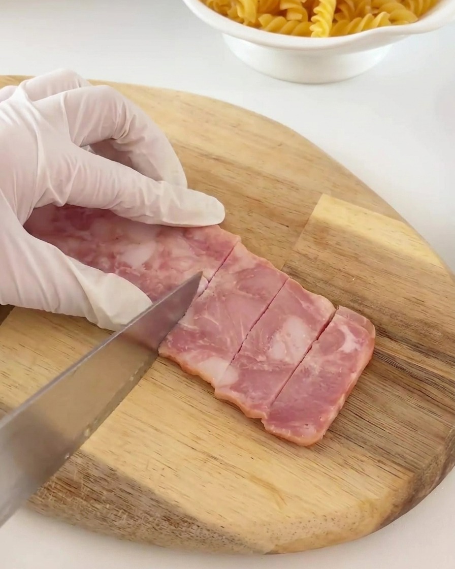Tiras de bacon siendo cortadas en pequeños trozos rectangulares consistentes sobre una tabla de madera.
