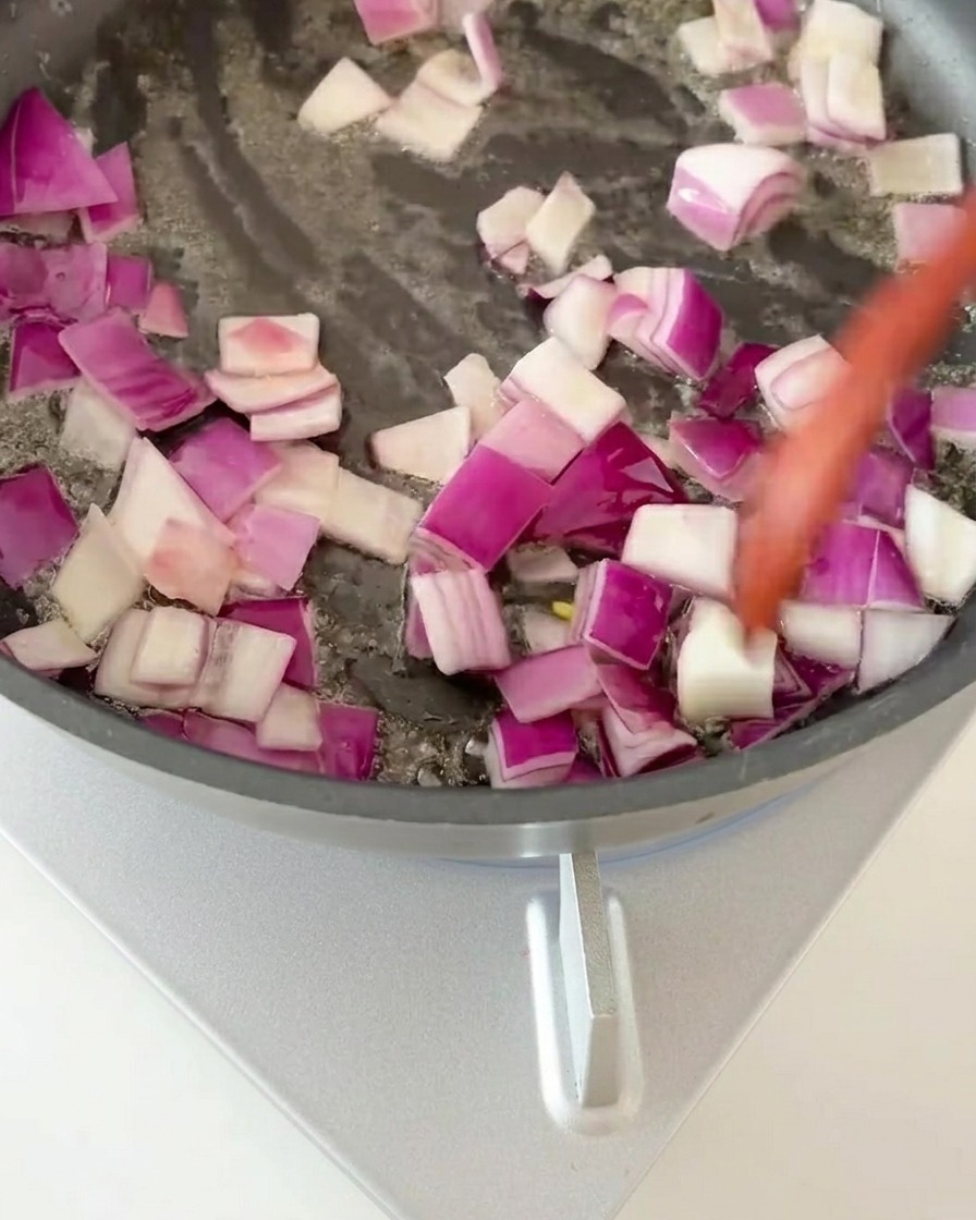 Cubitos de cebolla morada siendo salteados en una sartén caliente hasta que están fragantes.