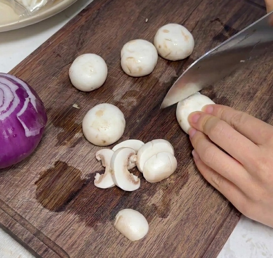 Champiñones blancos frescos cortados en láminas uniformes sobre una tabla de madera.