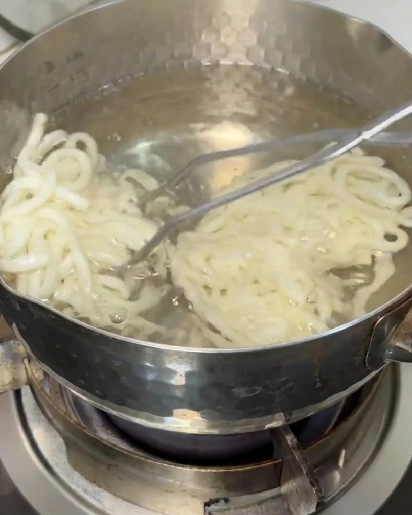 Fideos udon siendo retirados de una olla con agua hirviendo usando un colador.