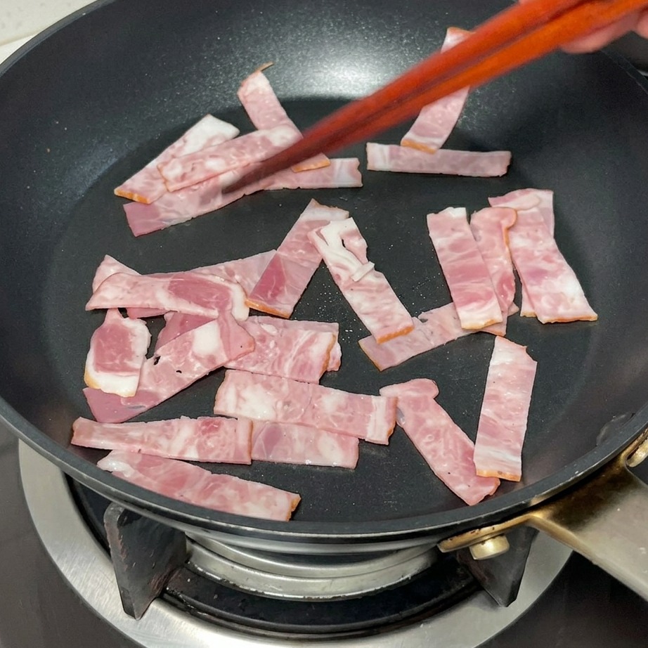 Tiras de bacon friéndose en una sartén hasta alcanzar un color dorado.