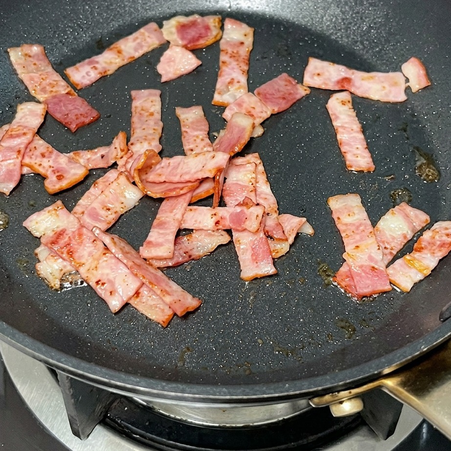 Una nuez de mantequilla derritiéndose en una sartén con trozos de bacon frito.