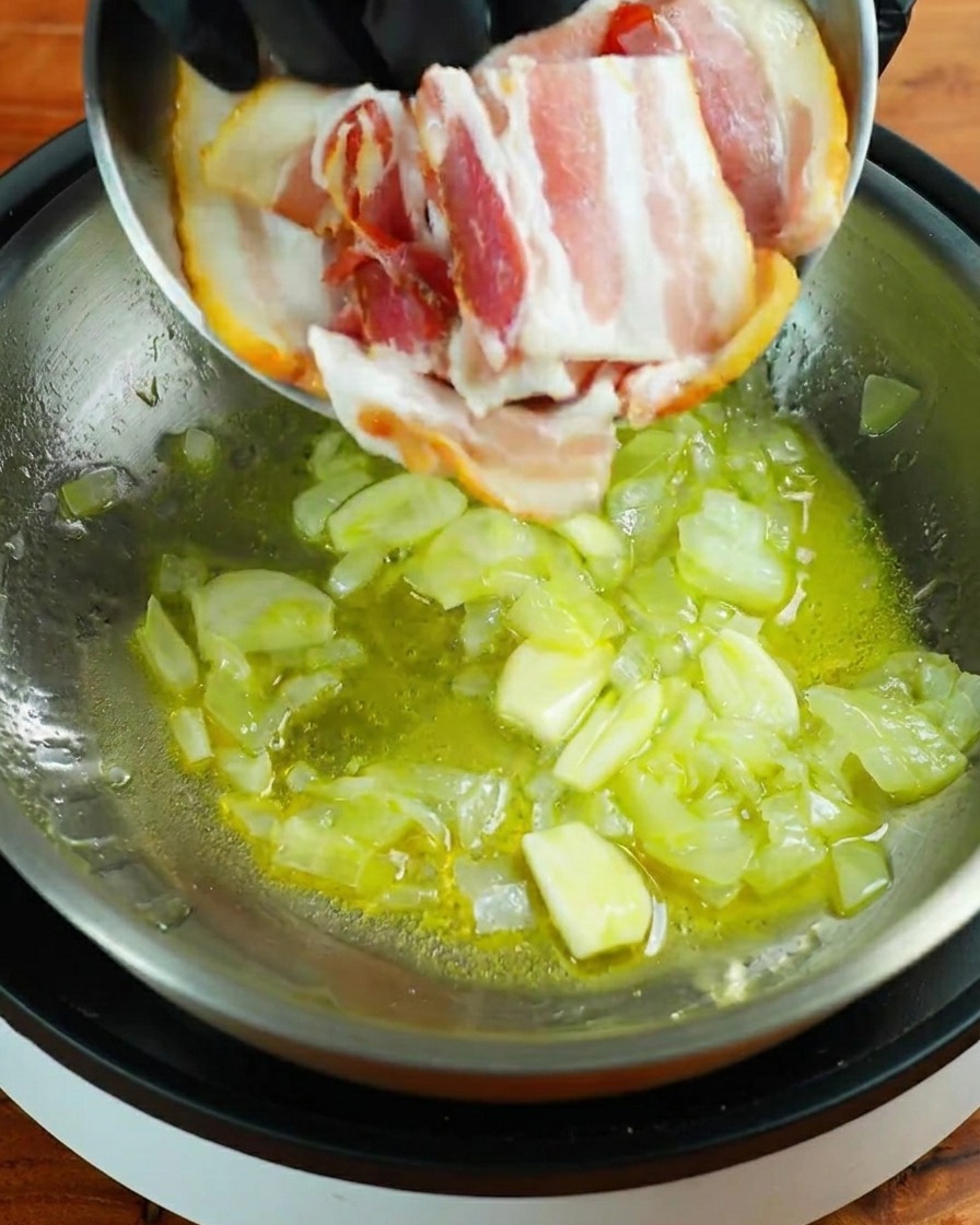 Tres tiras de bacon crudo siendo añadidas a una sartén con ajo y cebolla.
