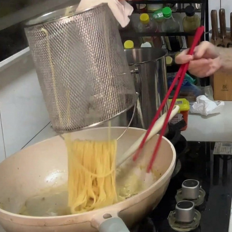 Espaguetis cocidos transfiriéndose a una sartén con la salsa cremosa de champiñones.