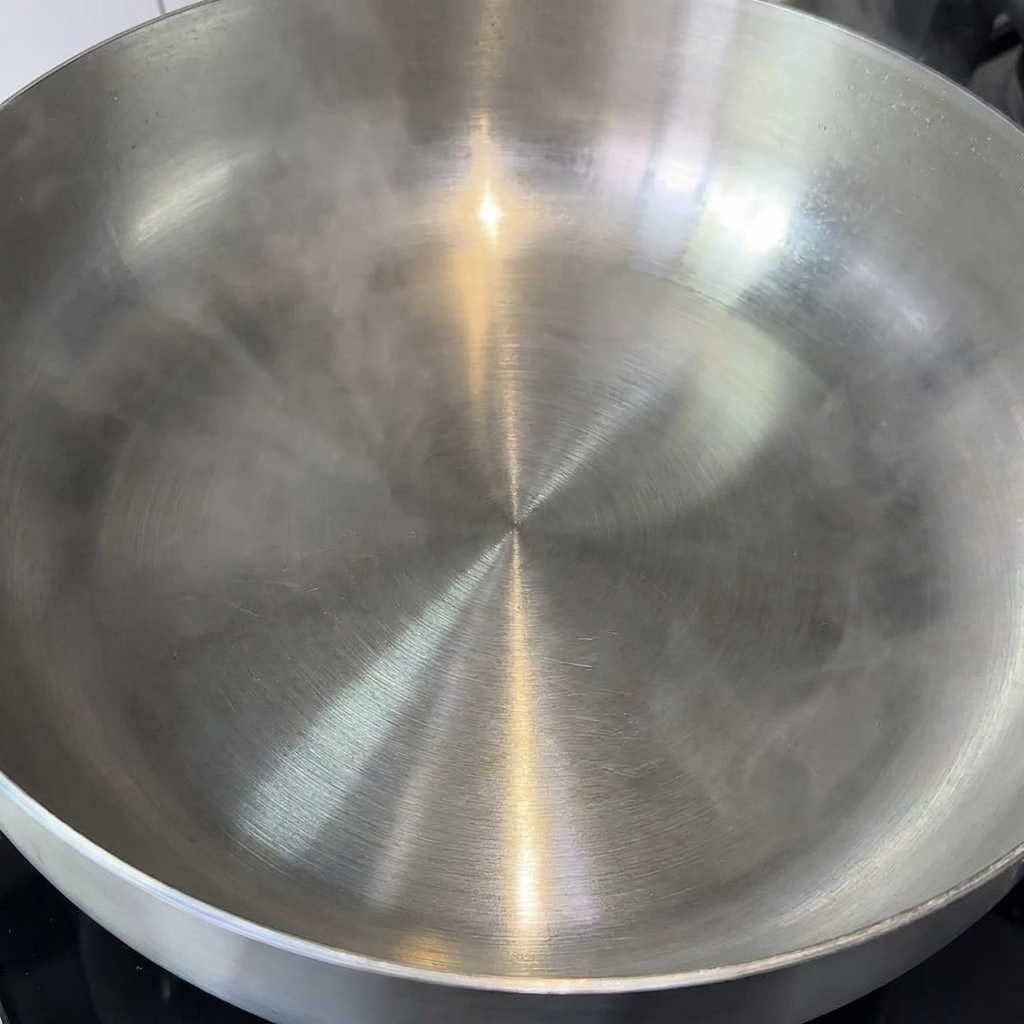 Un cubo de mantequilla derritiéndose en una sartén grande y limpia de acero inoxidable.