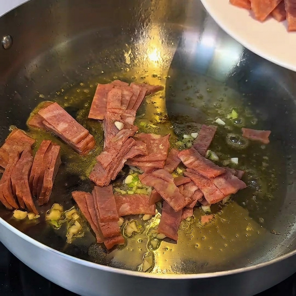 Trozos de ajo y tocino salteados en mantequilla derretida en una sartén de metal.