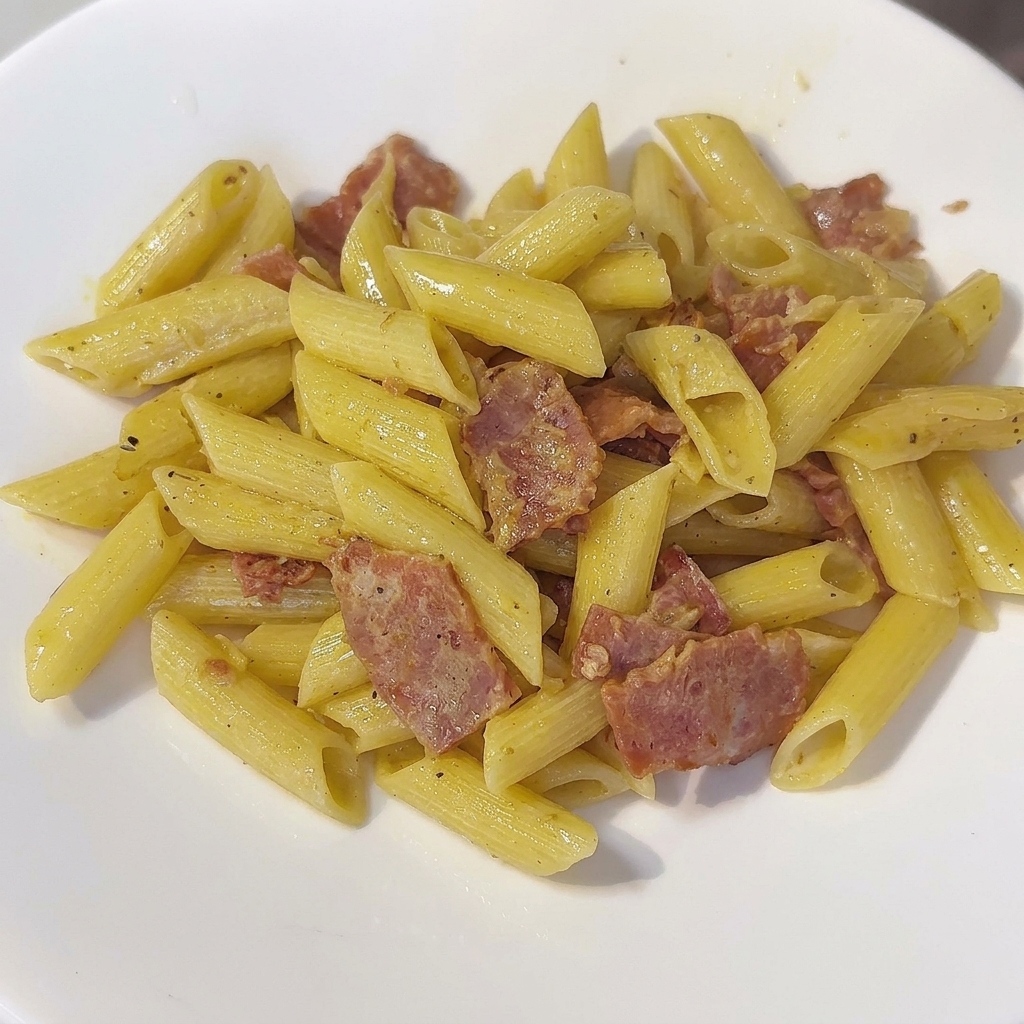 Una sartén de pasta penne cremosa siendo removida con una espátula.