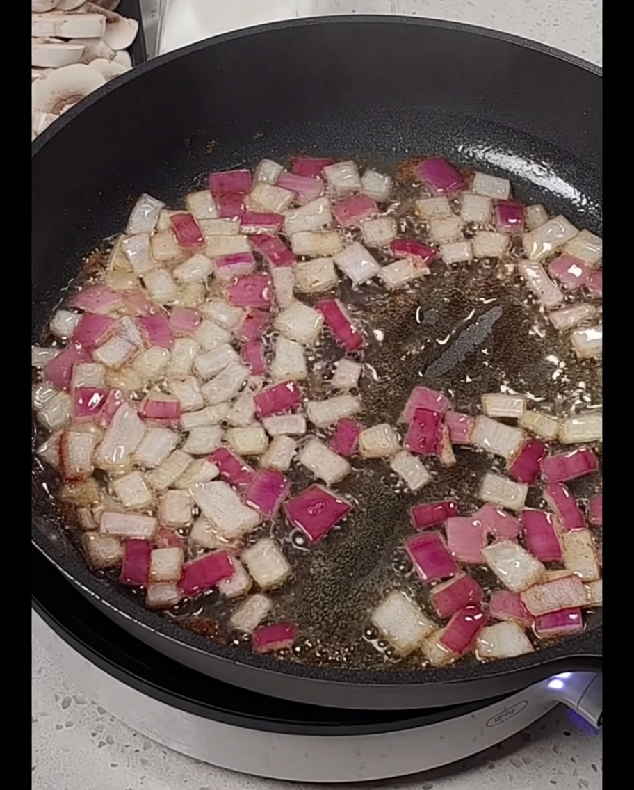 Tiras de bacon añadidas a una sartén con cebolla roja sofrita.