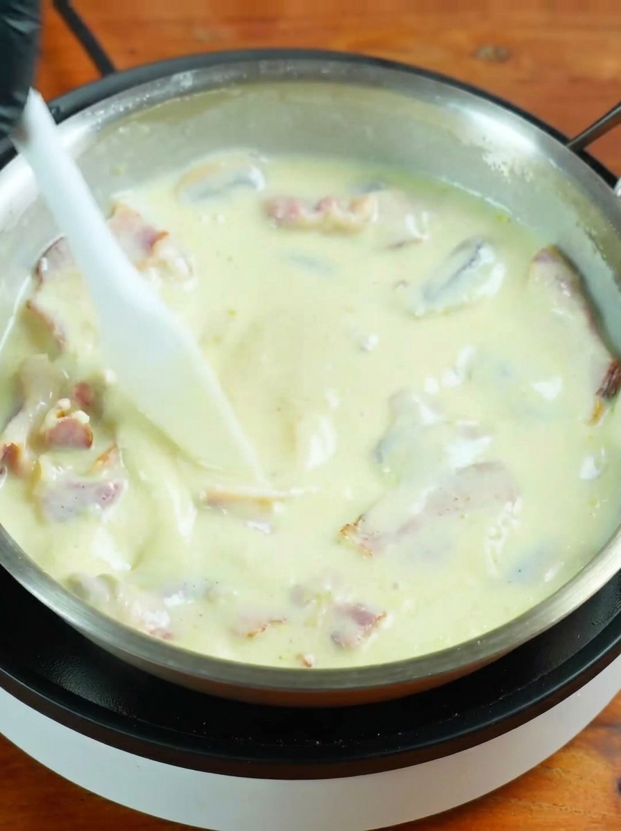 Espaguetis cocidos añadidos a una salsa cremosa burbujeante.